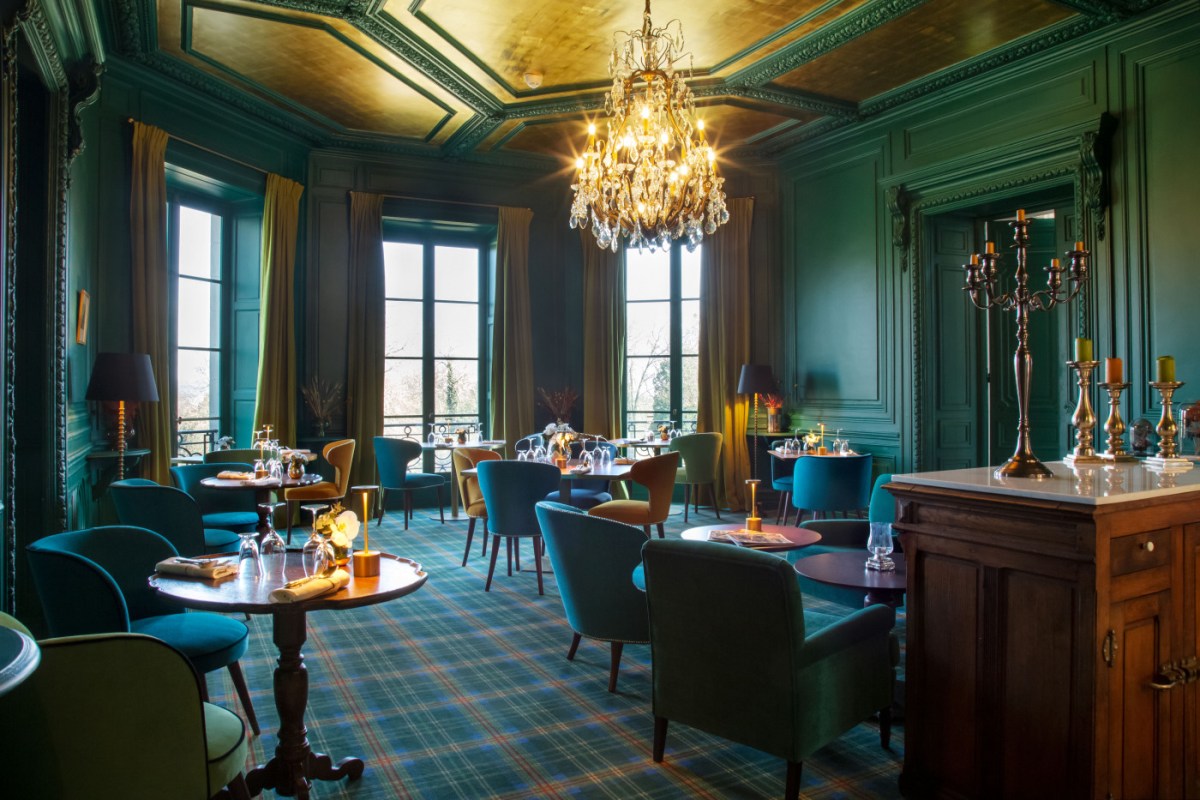 Elegant green dining room with chandelier, tartan carpet, and set tables by tall windows
