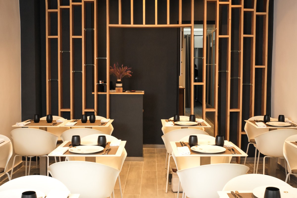 Dining room with wooden slatted dividers, dark walls, and set tables with white chairs