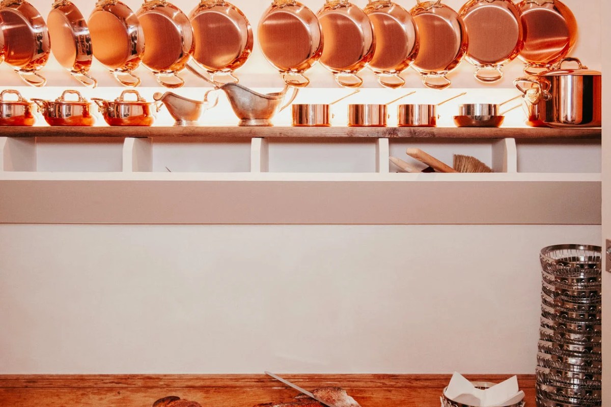 Shelf lined with polished copper pots and pans above a prep counter inside the restaurant