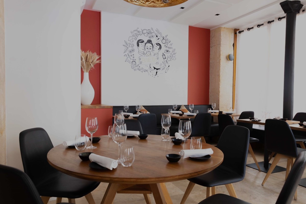 Baieta restaurant dining room with set wooden table, black chairs, wine glasses, and mural on wall