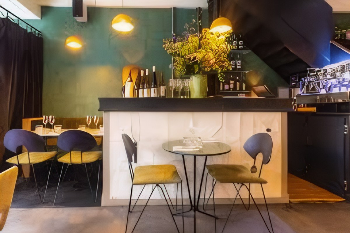 Restaurant bar area with small table, chairs, wine bottles, and flowers