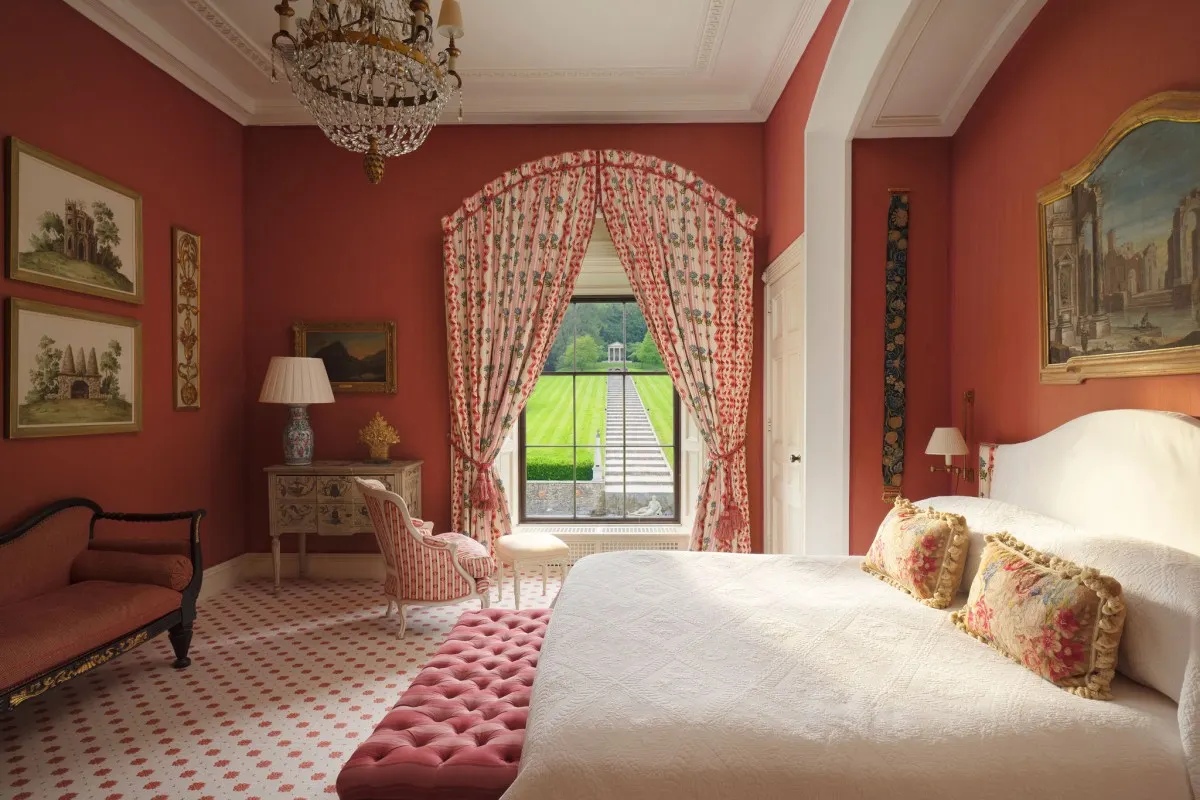 Elegant red-themed guest bedroom with four-poster-style bed and garden view through arched window