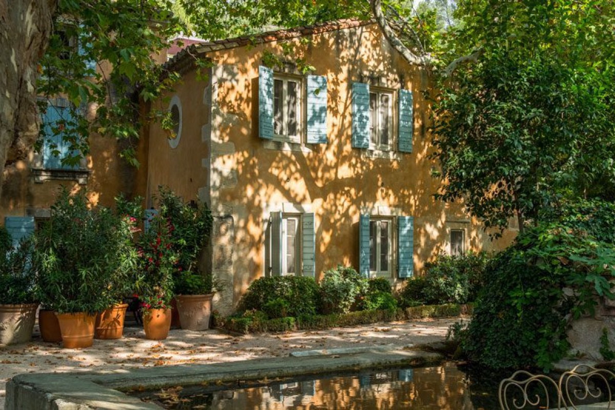 Provençal building facade with blue shutters, potted plants and reflecting pool under tree shade