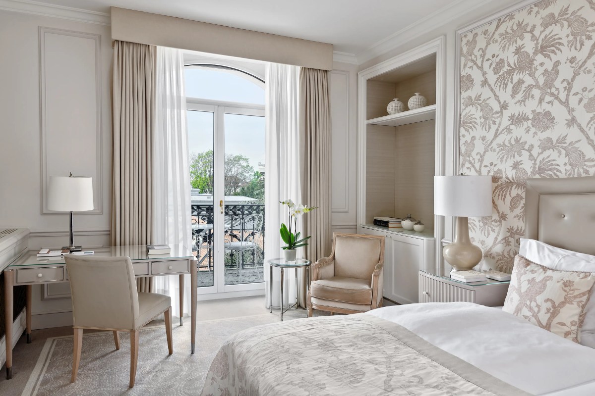 Elegant hotel guest room with floral wallpaper, desk, bed and balcony view