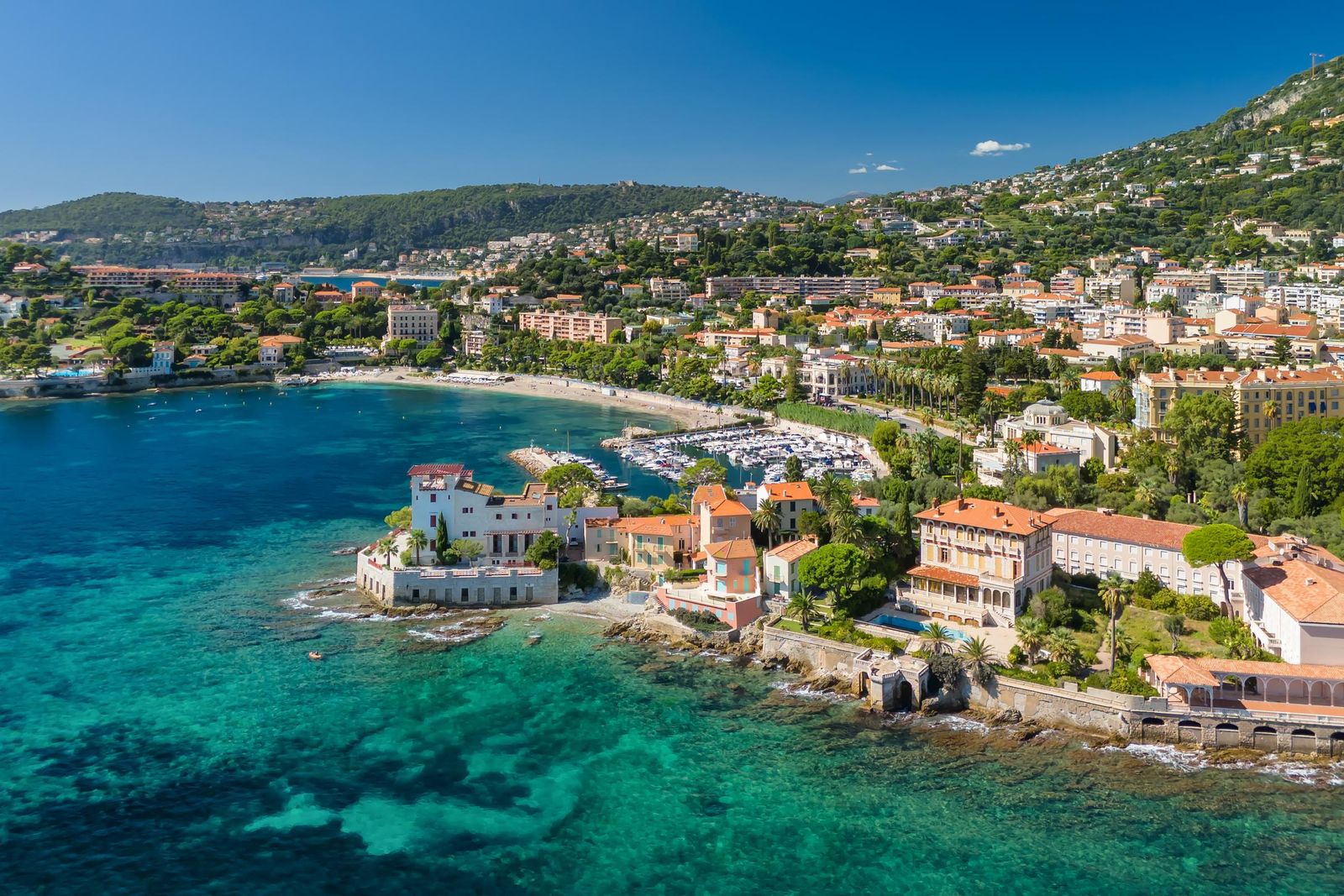 Beaulieu-sur-Mer from the air: villas on the point, the town along the shore and the turquoise bay below the hills