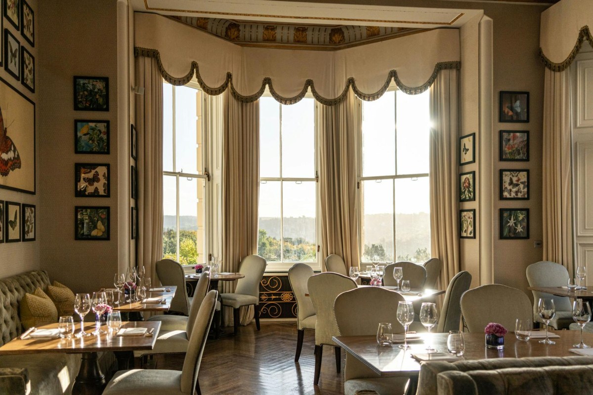Elegant hotel dining room with bay window, botanical prints, chandelier-lit tables and countryside view