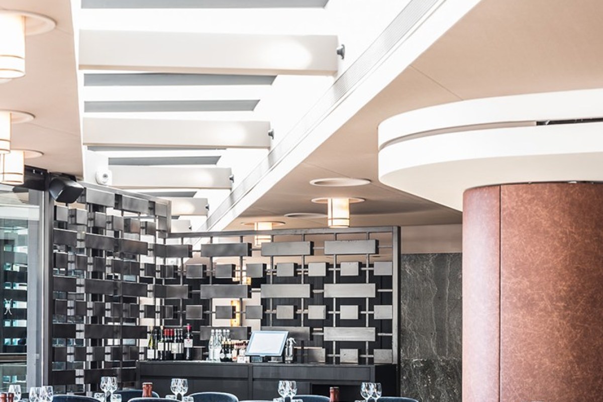Bright restaurant interior with decorative metal wall screen, bar area and set dining tables