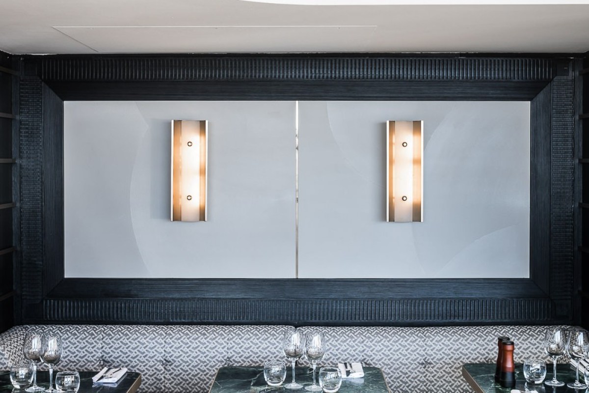 Dining room wall with modern sconces, framed panel, banquette seating and set tables with wine glasses