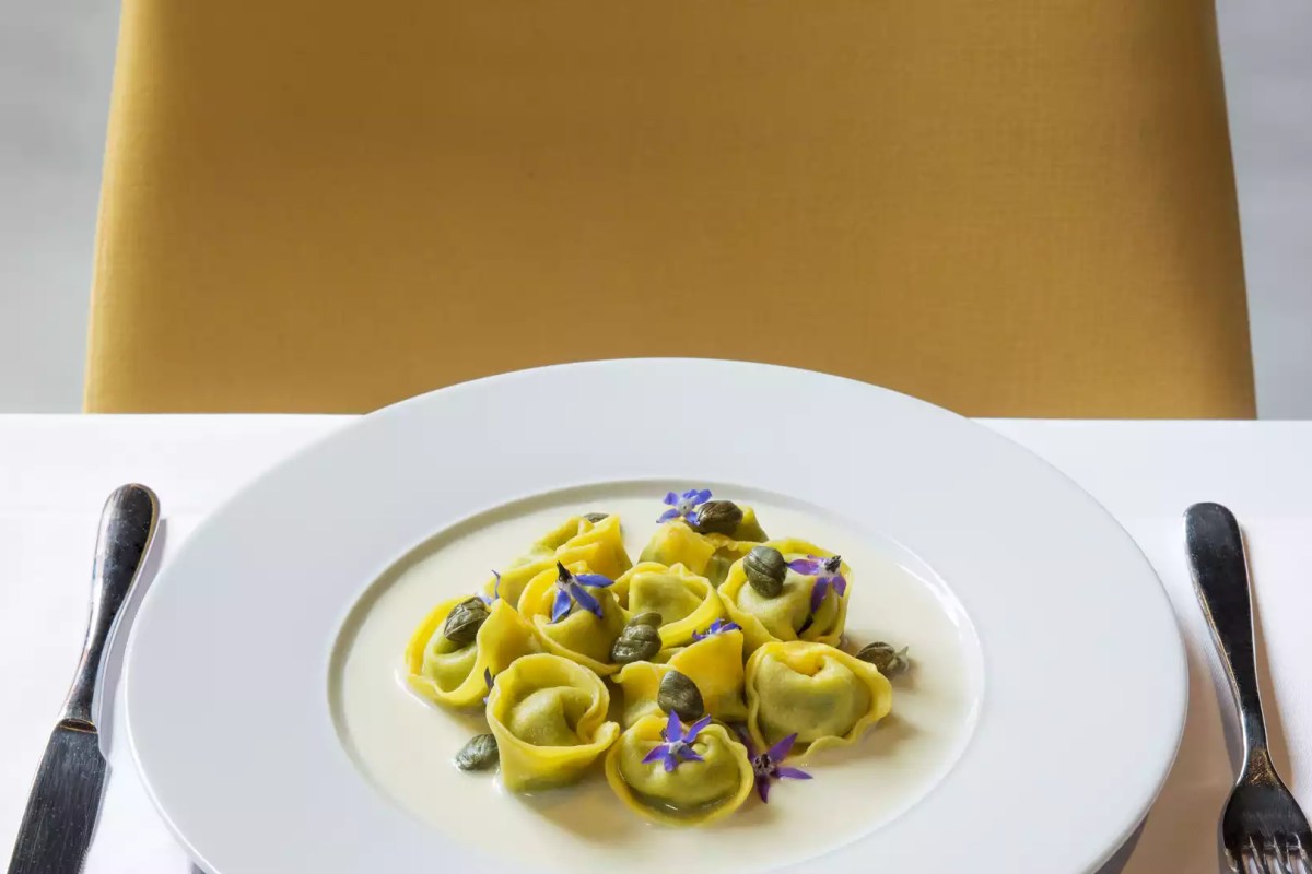 Plate of yellow tortellini with capers and purple edible flowers on white tablecloth