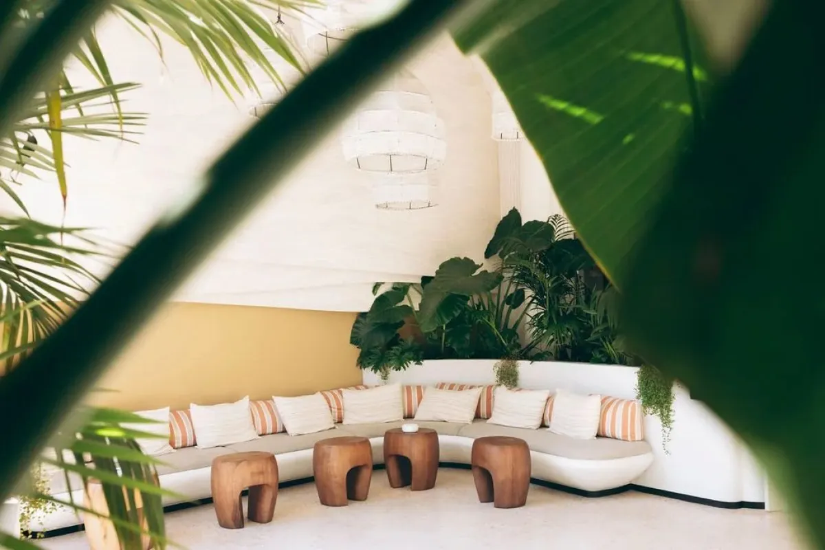 Tropical lounge area with curved sofa, striped cushions and wooden stools framed by palm leaves