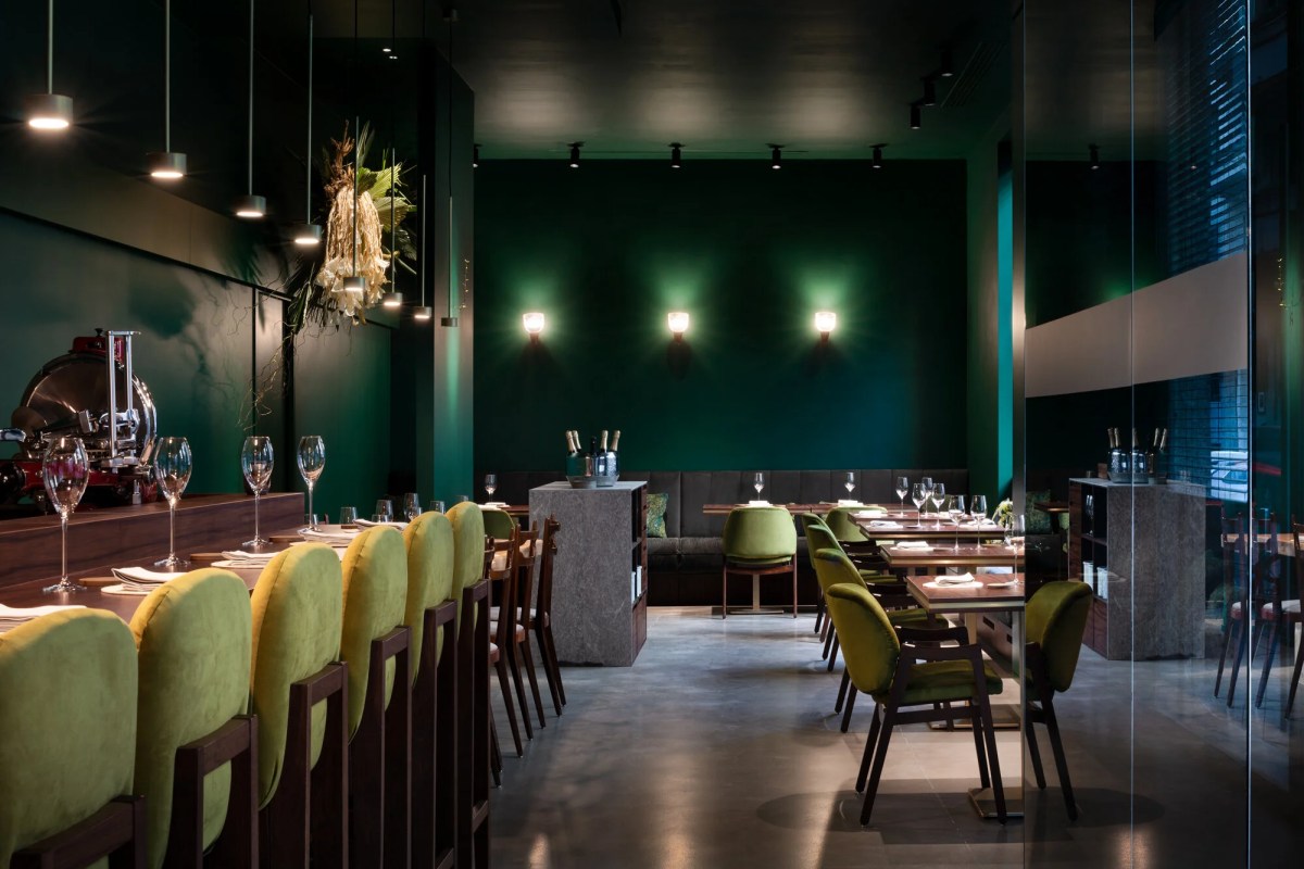 Restaurant dining room with green walls, velvet chairs, wine glasses and set tables