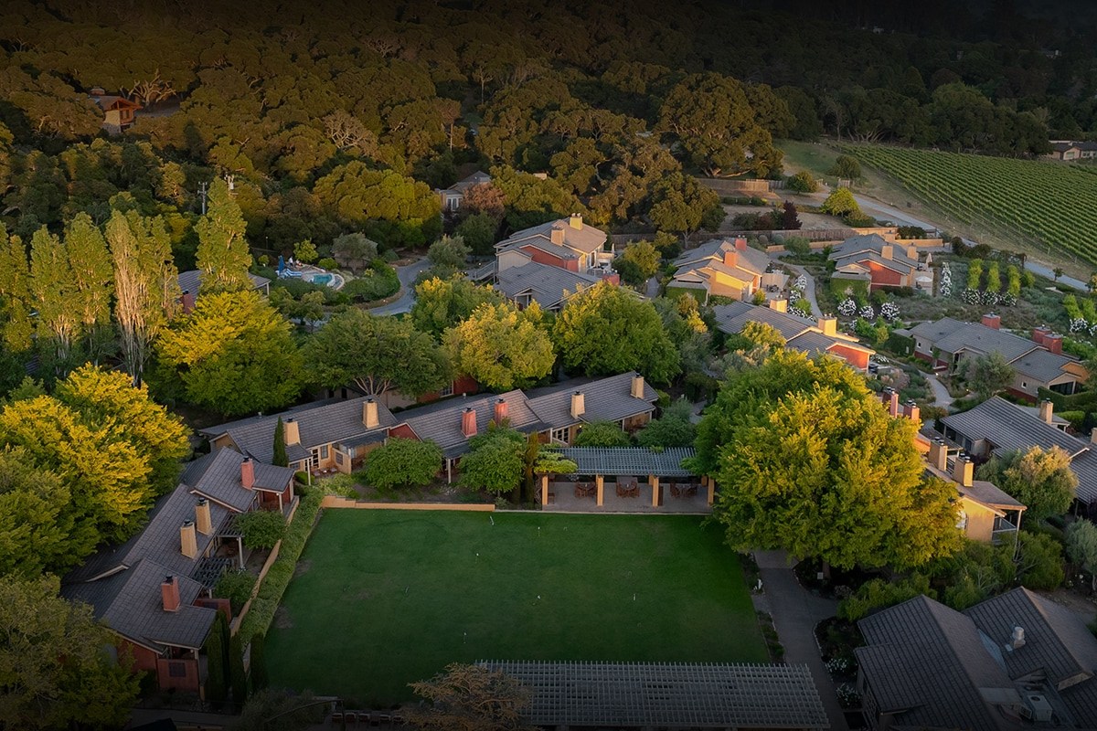 Aerial view of Bernardus Lodge & Spa cottages with lawn, pool and vineyard at golden hour