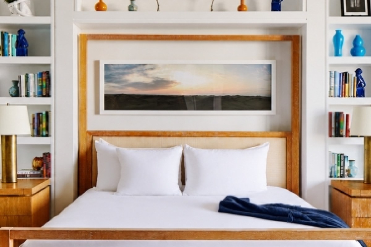 Hotel bedroom with wooden headboard, white pillows, and bookshelf decor above the bed