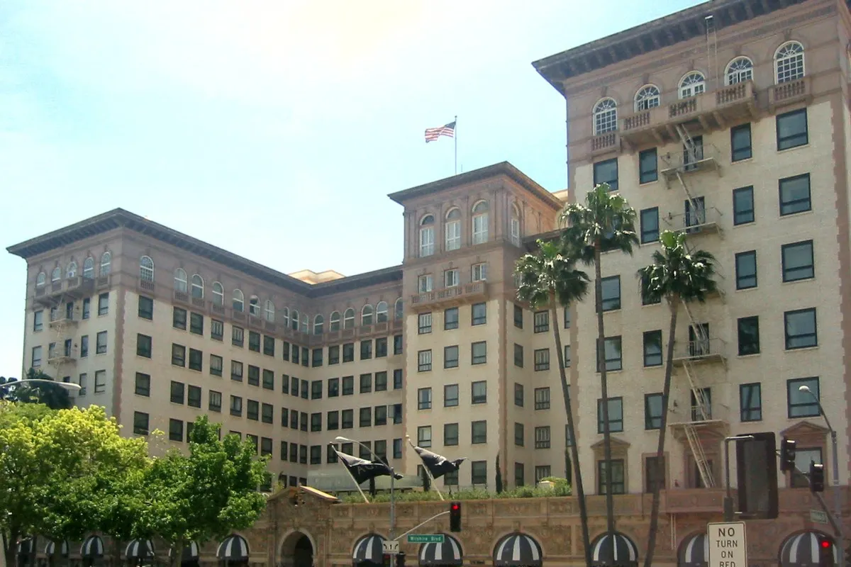 Beverly Wilshire hotel façade with palm trees and American flag under clear blue sky
