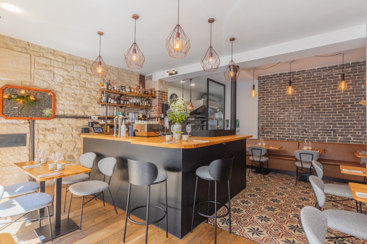 Interior dining room with bar counter, stone wall, exposed brick, pendant lights and patterned tile floor at Biscotte