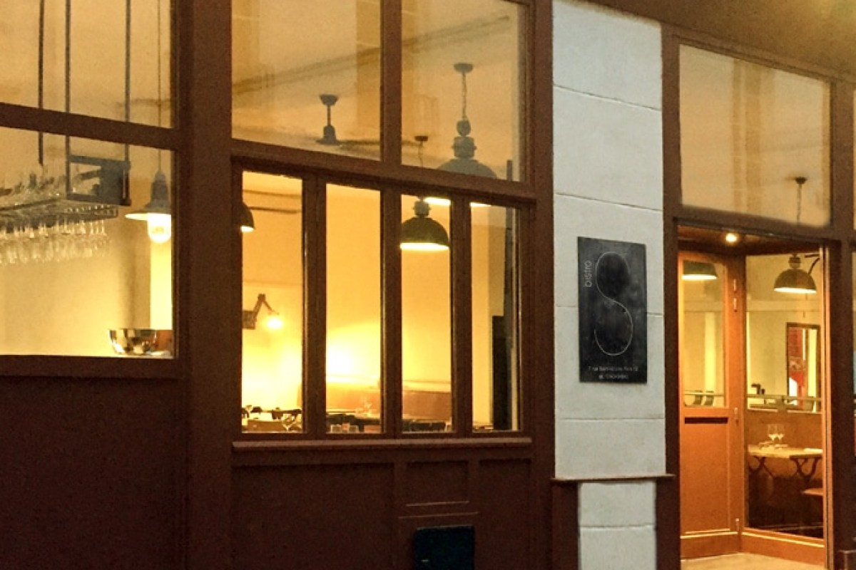 Exterior entrance of Bistro S at night, showing illuminated dining room through windows and signage