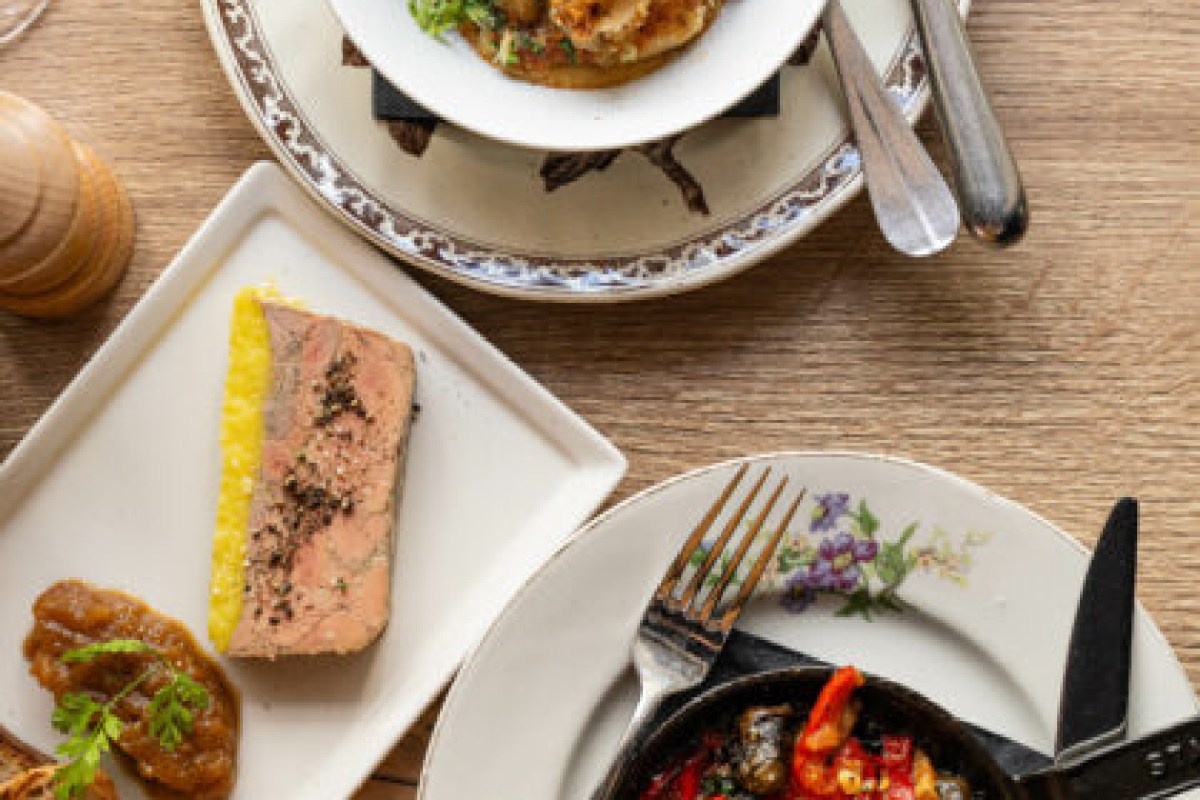 Overhead view of plated dishes including foie gras terrine, shrimp skillet, and meat dish on a wooden table