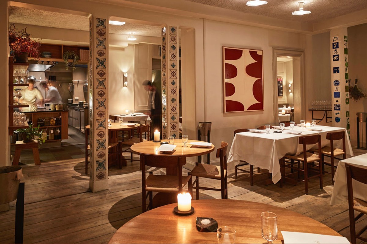 Cozy dining room with tiled columns, wooden tables, candles, and open kitchen in background.