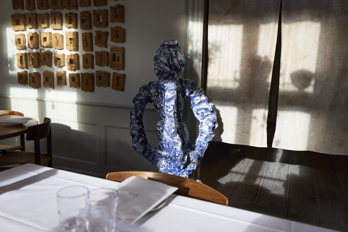 Abstract blue ceramic sculpture on a dining table with sunlight and shadow patterns on wall.