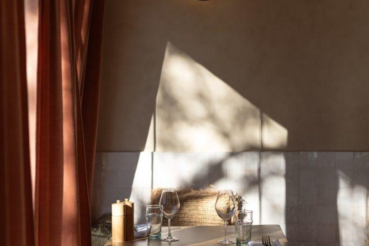 Laid restaurant table with wine glasses, water glasses, pepper mill, and dramatic afternoon light casting shadows on wall