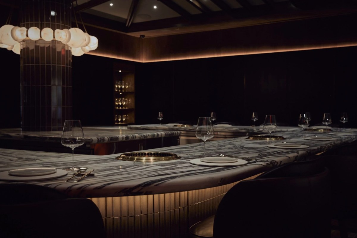 Dim, moody dining room with curved marble bar counter, wine glasses and place settings, pendant light fixture