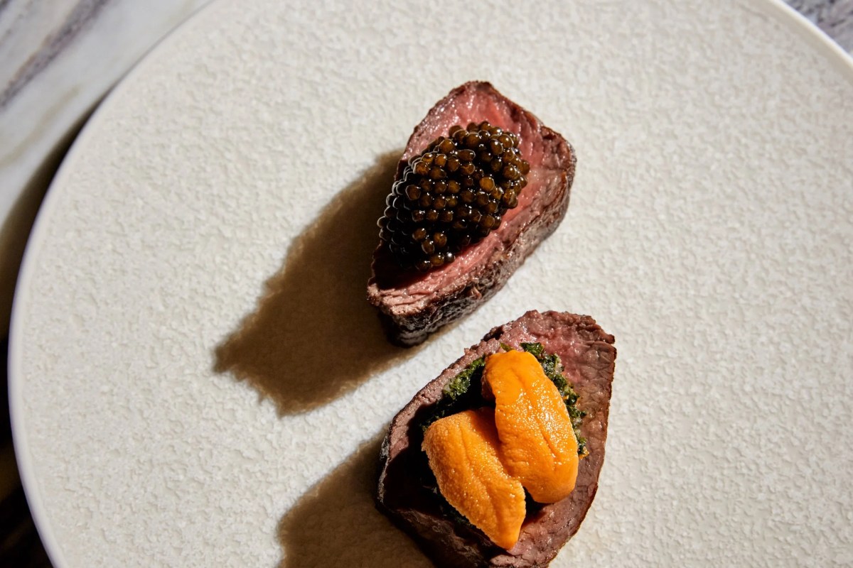 Two seared meat bites on a plate, one topped with caviar and one with uni and greens