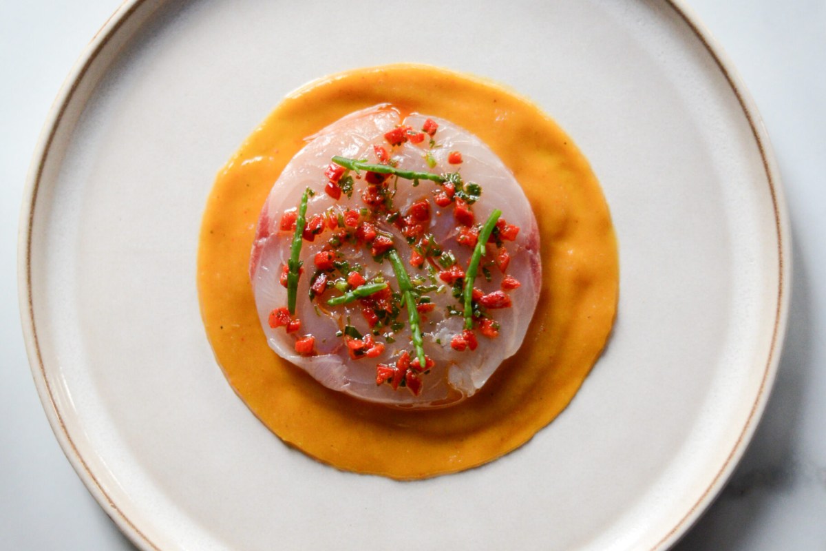 Top-down view of a plated dish with thin sliced fish, orange sauce swirl, and herb garnish