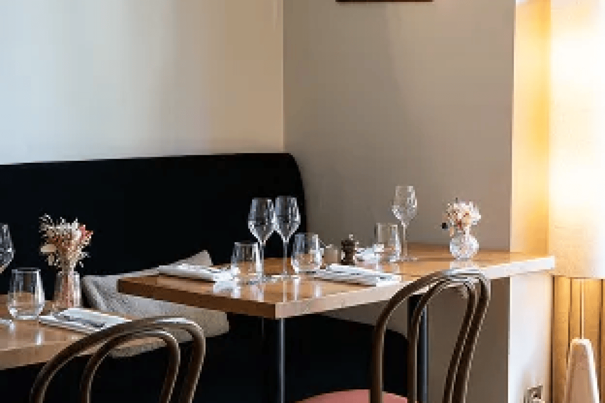 Restaurant dining room with a set wooden table, wine glasses, small flower vases, and bentwood chairs