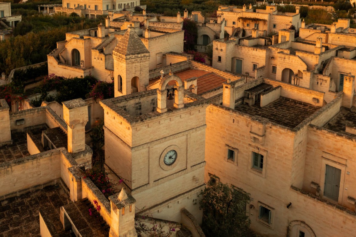 Aerial view of Borgo Egnazia's stone buildings and bell tower at golden hour, with a clock and rooftop terraces.