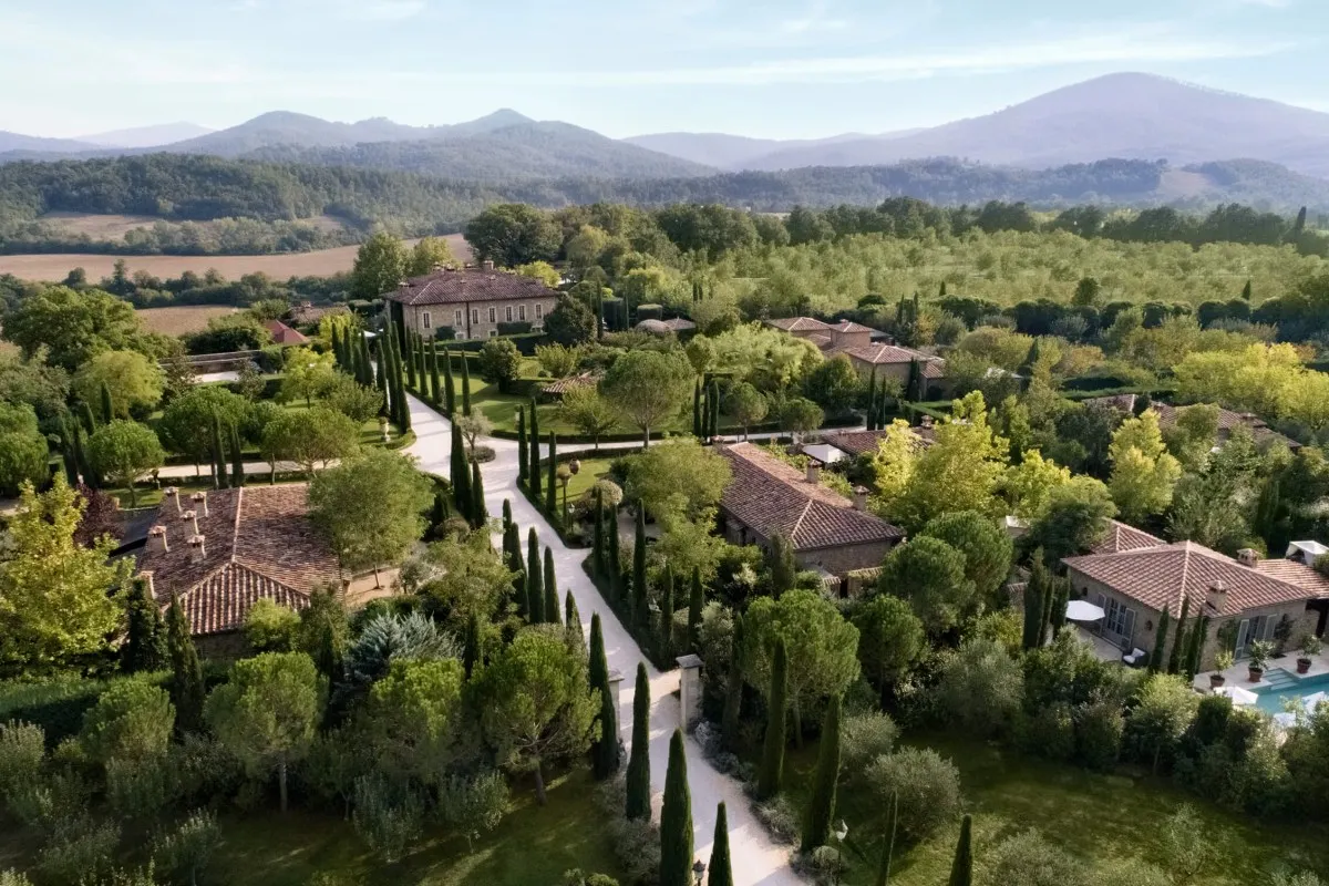 Aerial view of Borgo Santo Pietro's stone buildings, gardens, cypress-lined paths and pool, with Tuscan hills in the background