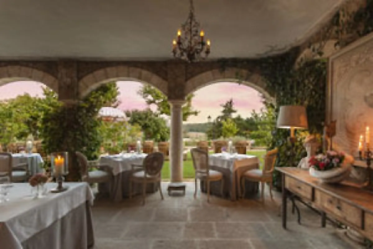 Elegant covered terrace with stone arches, dining tables set with white linens, overlooking gardens at dusk.