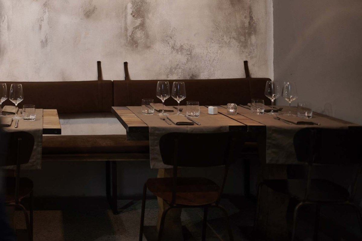 Interior dining area with leather banquette seating, wooden tables set with wine glasses and napkins against a textured wall