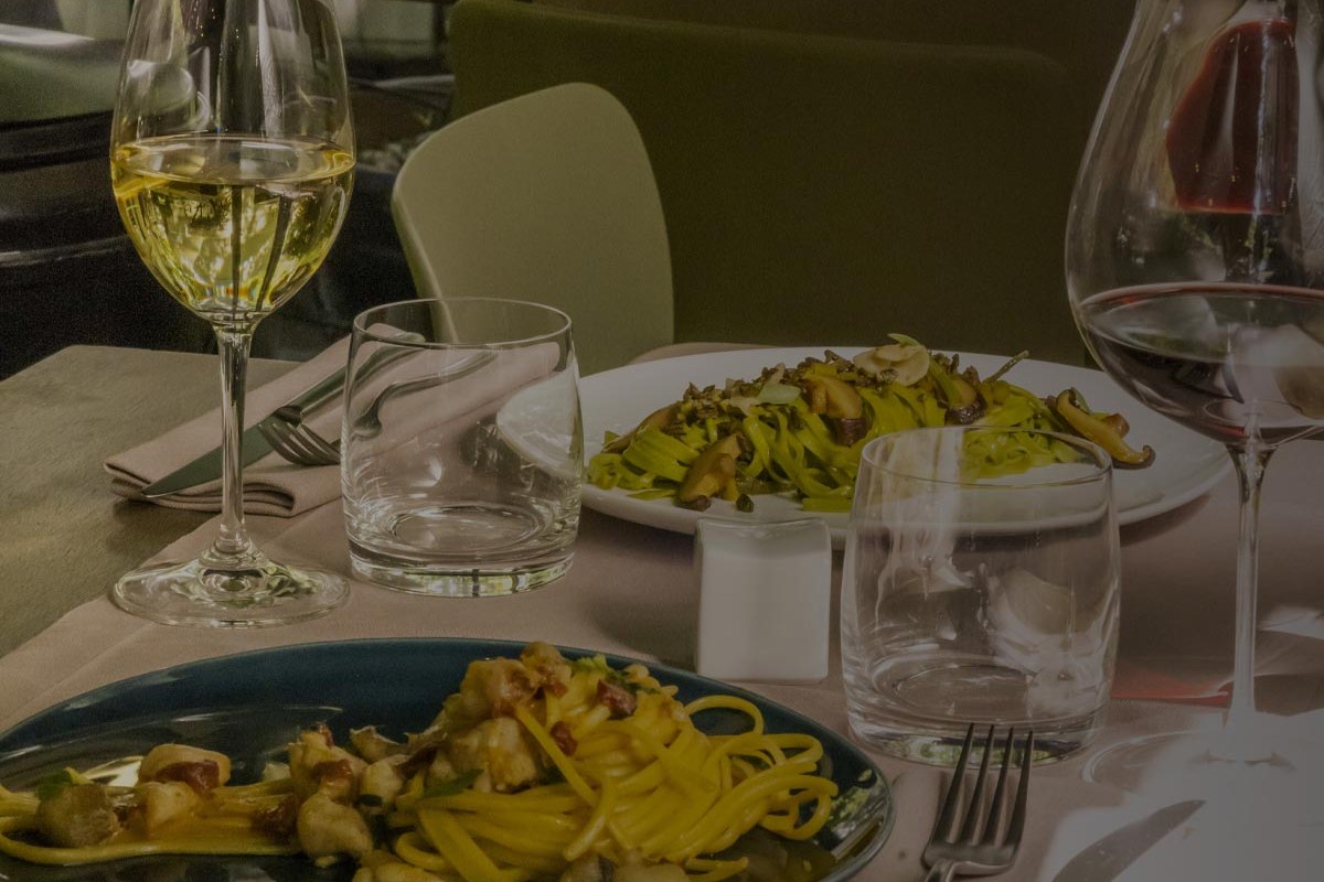 Restaurant dining table set with two pasta dishes, wine glasses and a carafe, green chair in background