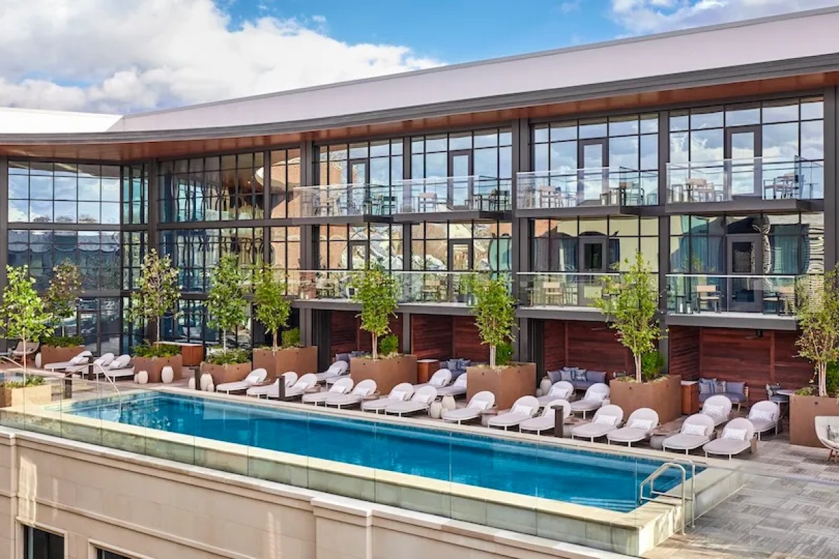 Rooftop pool with lounge chairs beside the glass-and-brick facade of Bowie House hotel