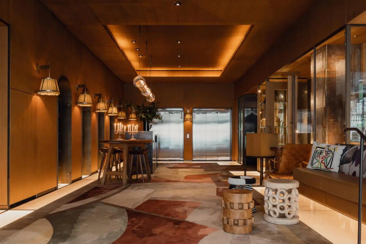 Warm-toned hotel lobby/lounge with wood paneling, seating, and sculptural stools