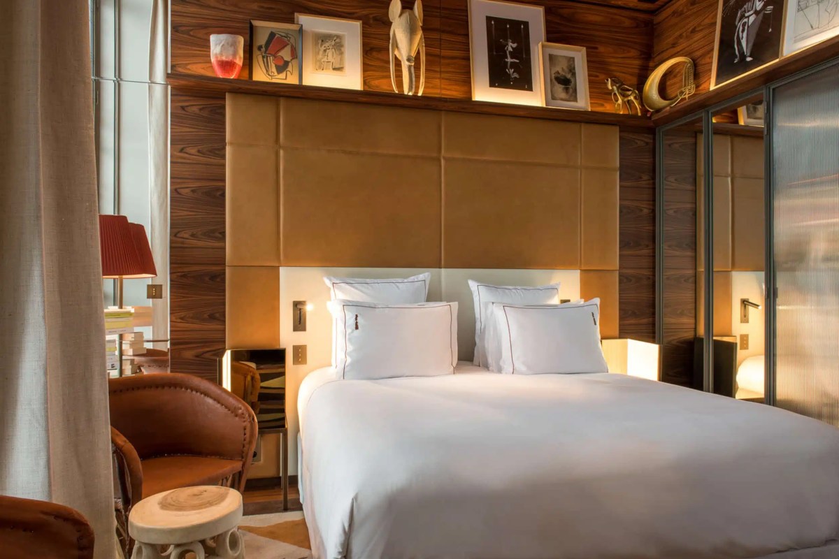 Hotel guest room with large bed, leather headboard, wood paneling and art display shelf