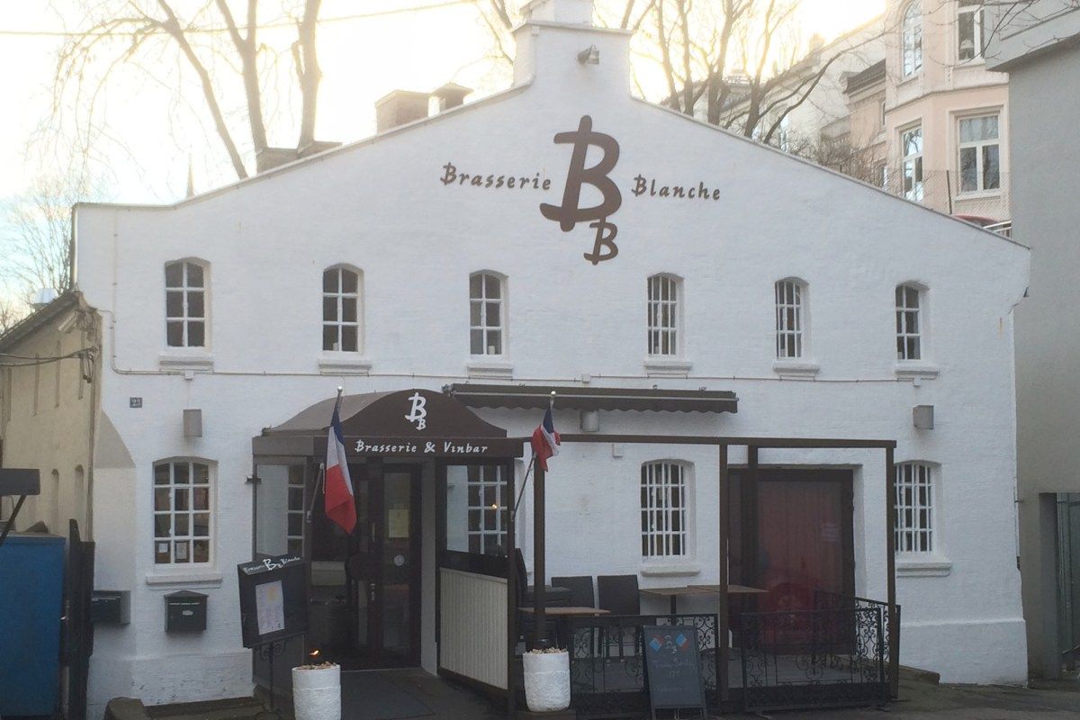 White building exterior of Brasserie Blanche with terrace seating and French flags at entrance