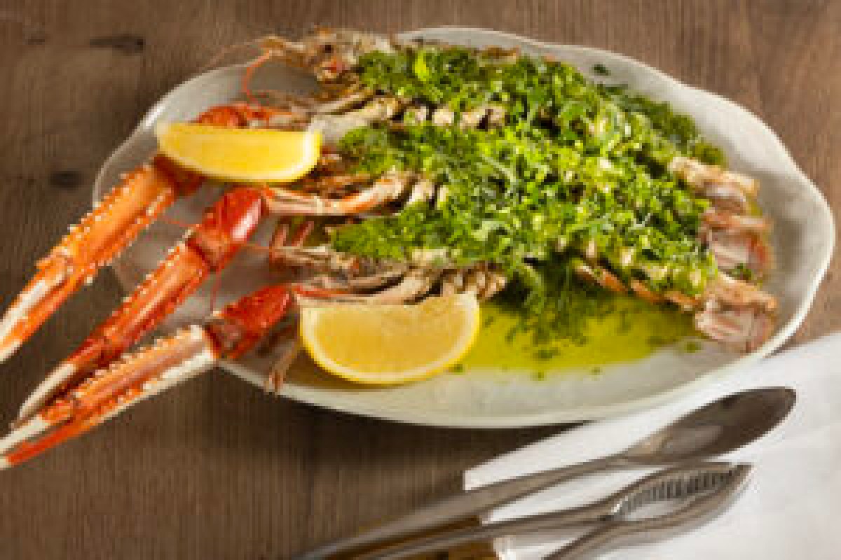 Grilled langoustines topped with green herb butter, lemon wedges, on a white oval plate