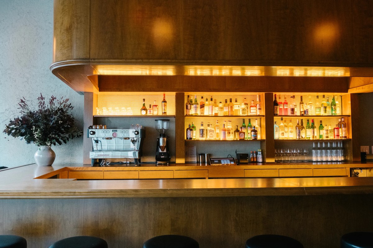 Close-up of wooden bar counter with illuminated liquor shelves and flowers