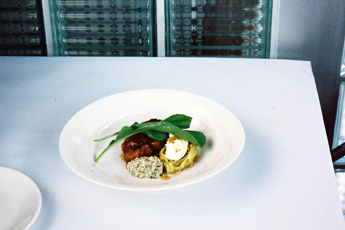 Plated dish with pasta, meatballs, arugula, and burrata on white table