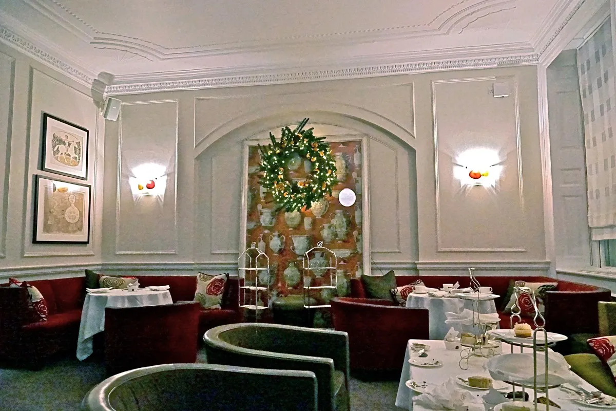 Elegant hotel tea room with red banquette seating, set tables, and decorative wall niche