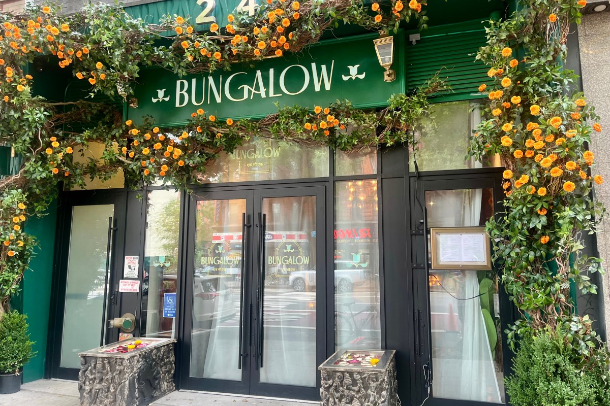 Exterior storefront of Bungalow restaurant in NYC with green facade, orange flowering vines, and glass doors