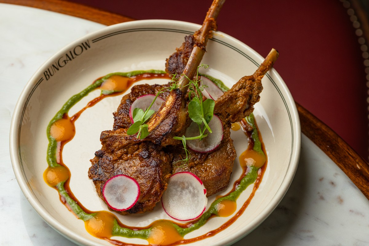 Plate stamped BUNGALOW with lamb chops, radish slices, and herb and spice sauces on a marble table