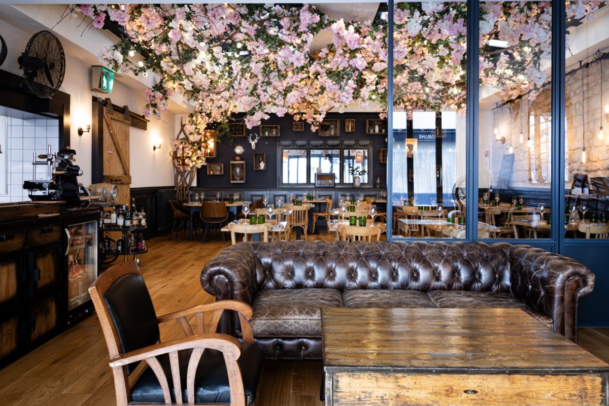Interior view through glass partition showing dining area, bar, and cherry blossom decor with street visible outside