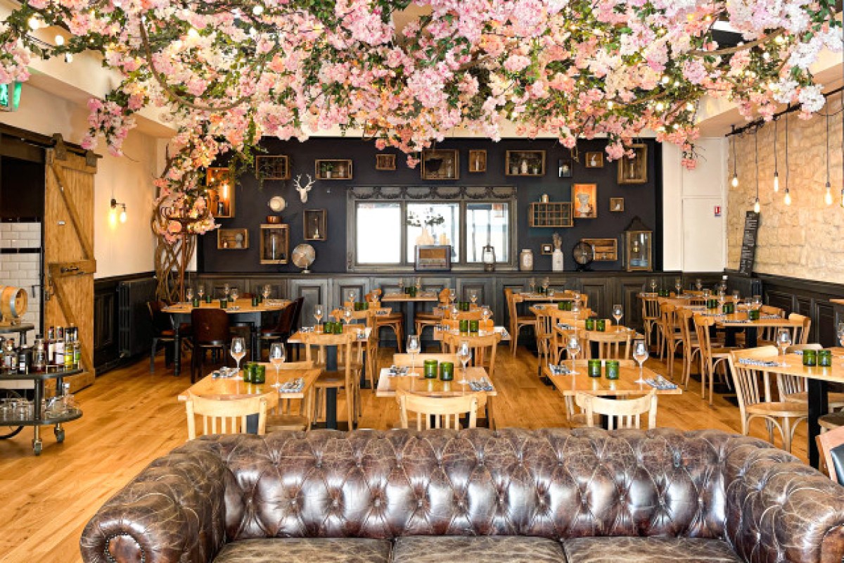 Restaurant dining room with wooden tables, leather sofa, and cherry blossom ceiling decor