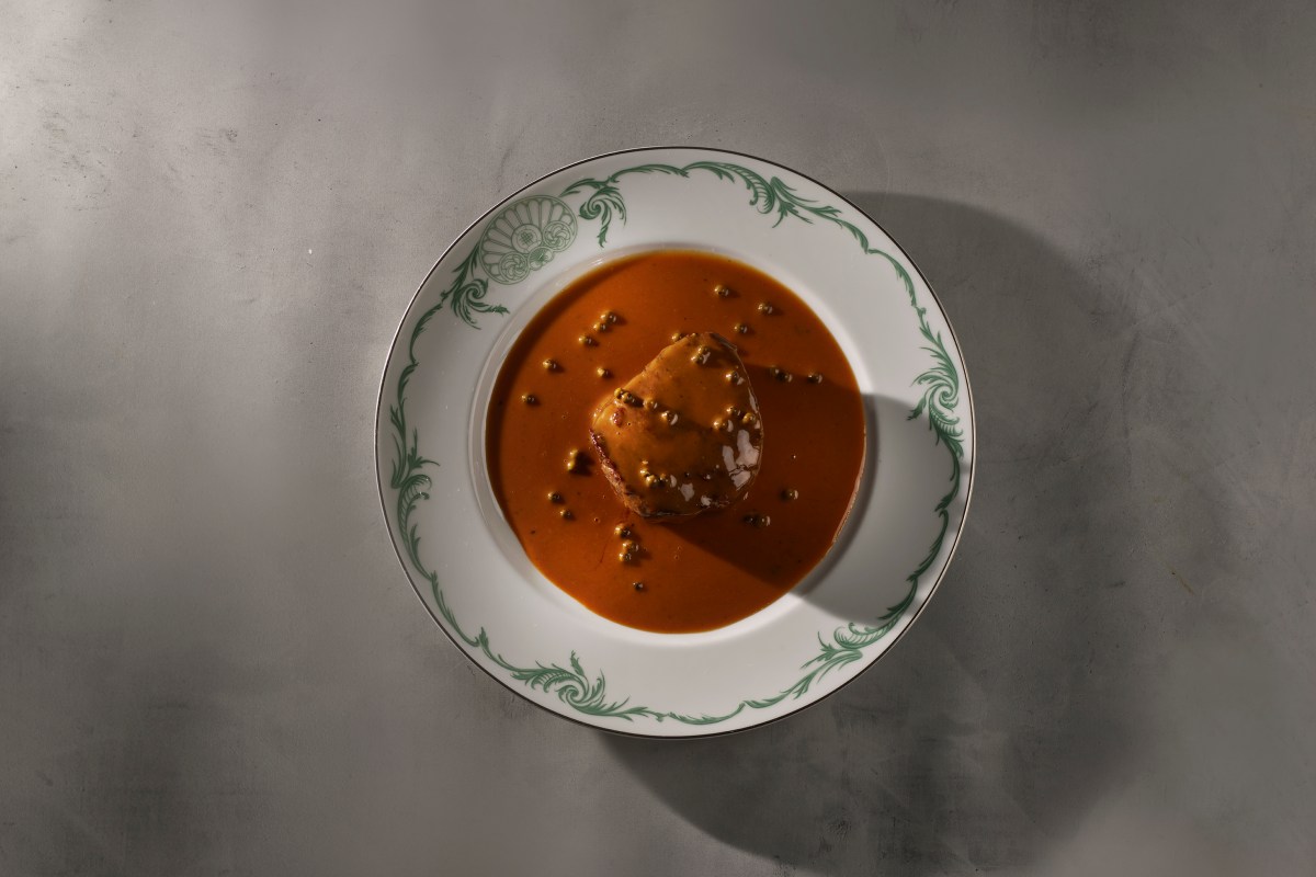 Overhead shot of a dish with a round food item in orange sauce dotted with green peppercorns
