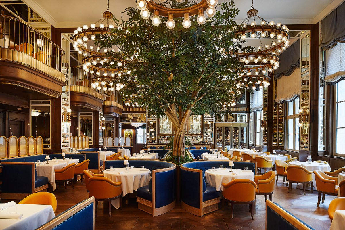Elegant restaurant dining room with blue booths, yellow chairs, and a tree feature under chandeliers
