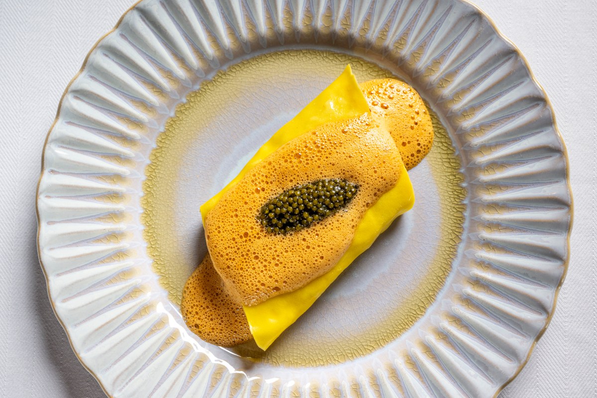 Elegant plated dish with yellow pasta, foam, and caviar on ornate white plate