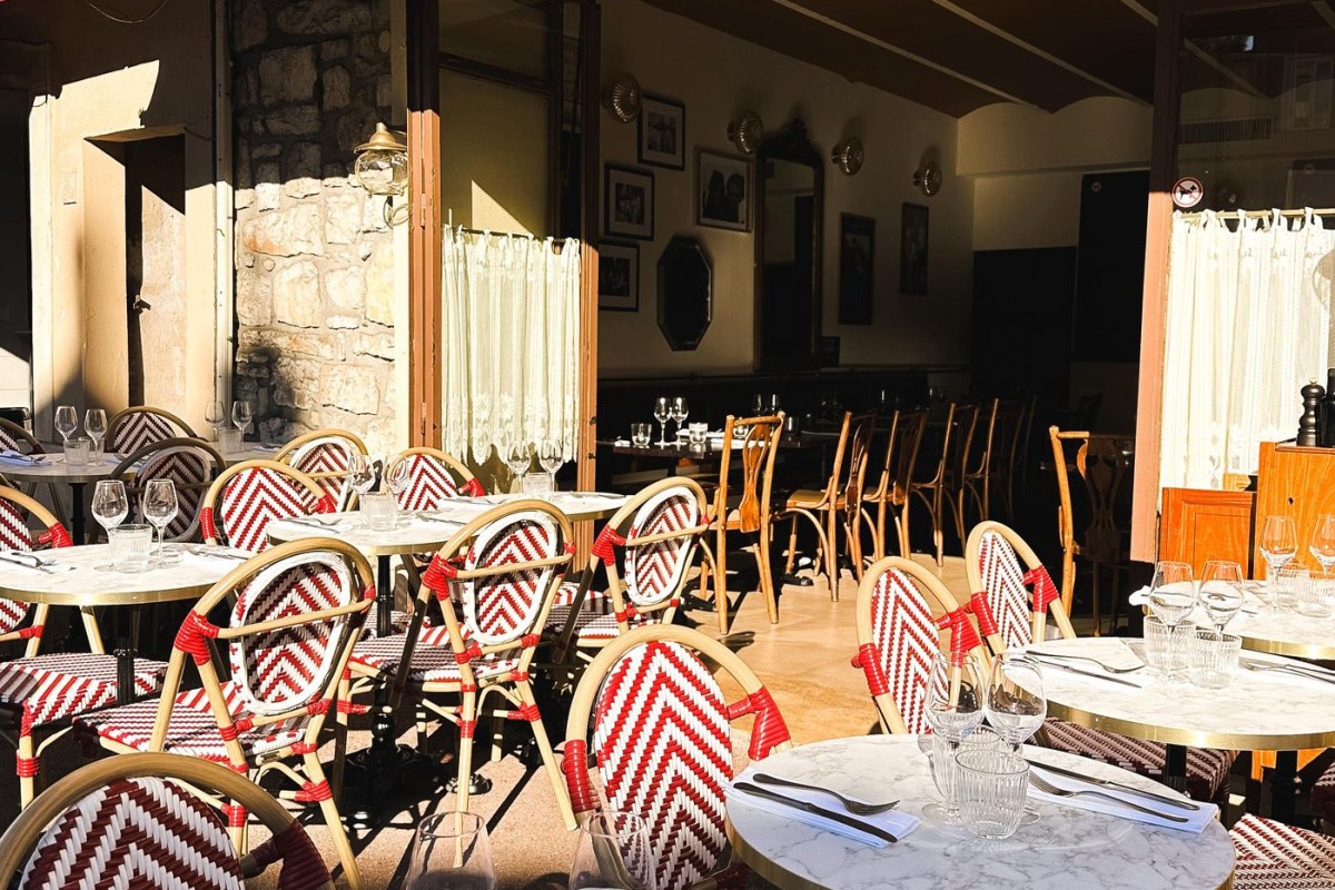 Restaurant terrace with red-and-white woven bistro chairs and marble tables, interior dining room visible beyond