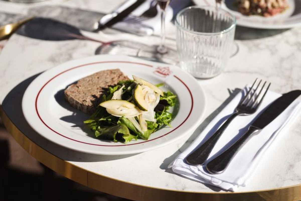 Terrine slice with mixed green salad and pear on red-rimmed plate, set on marble bistro table